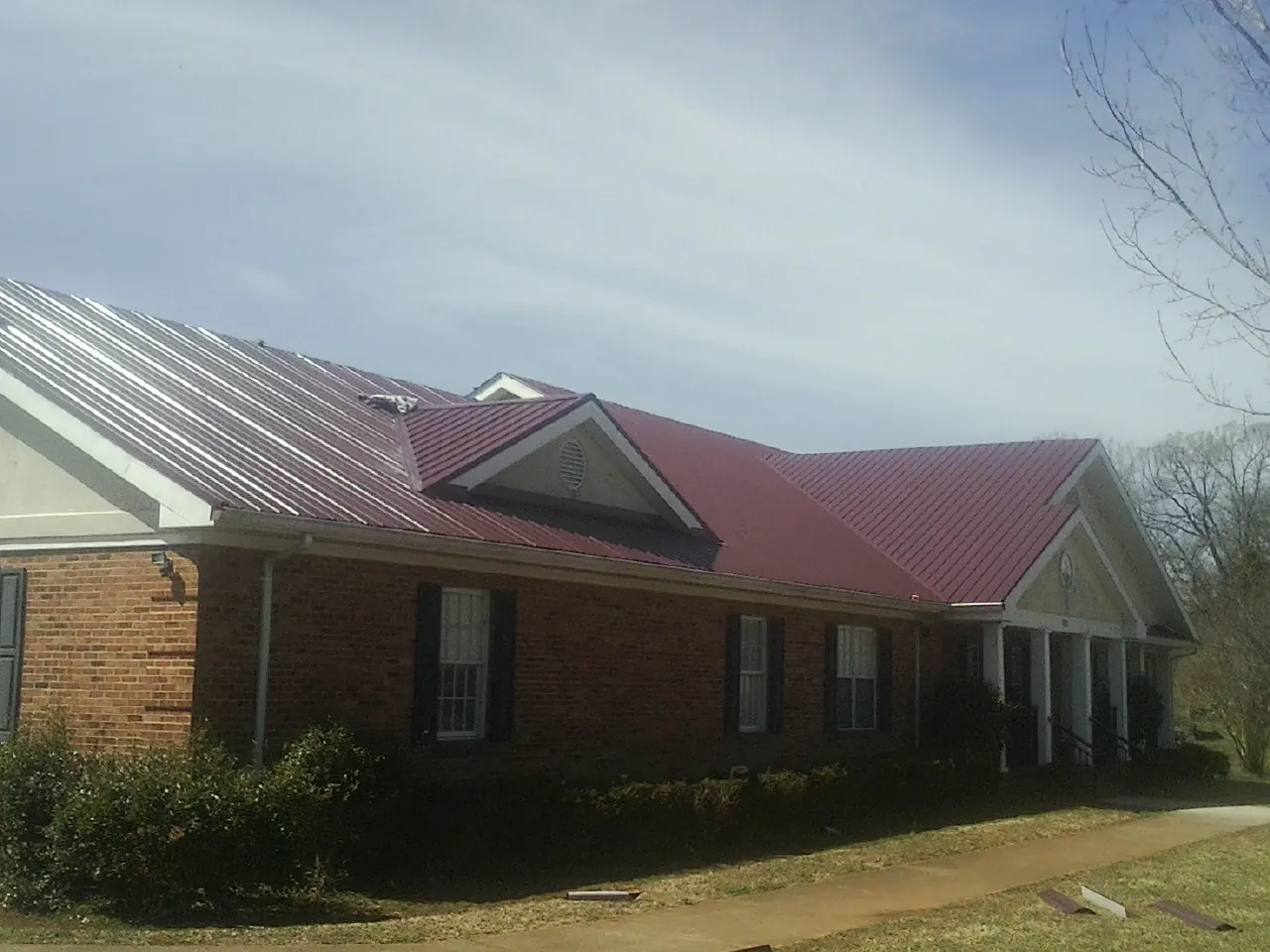 Red metal roof with gabled entries on a long brick building, from a Hail Damage Roof Repair job in York